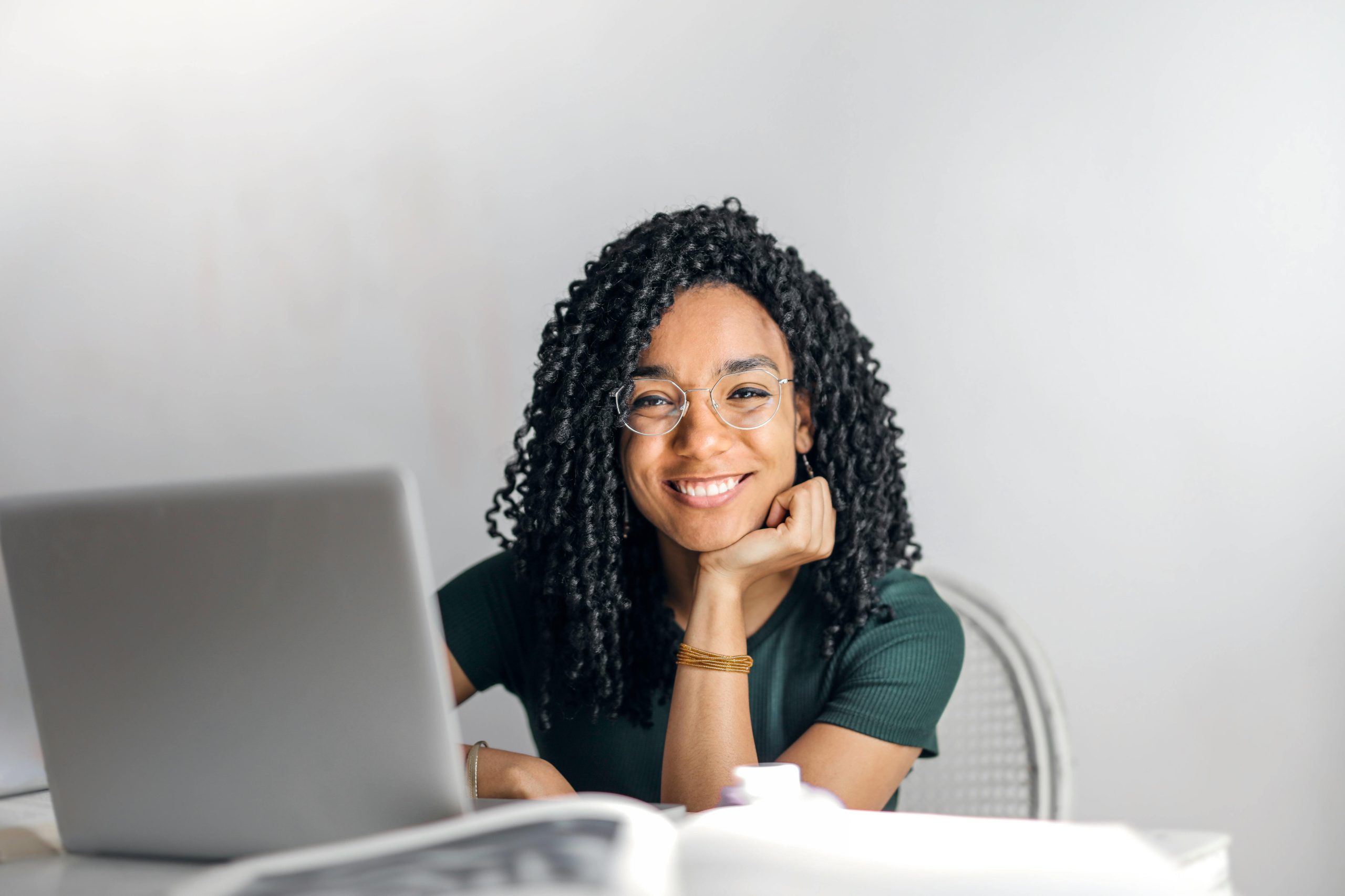 pexels-photo-3769021-3769021 Joyful businesswoman with curly hair smiling at camera while using laptop indoors.